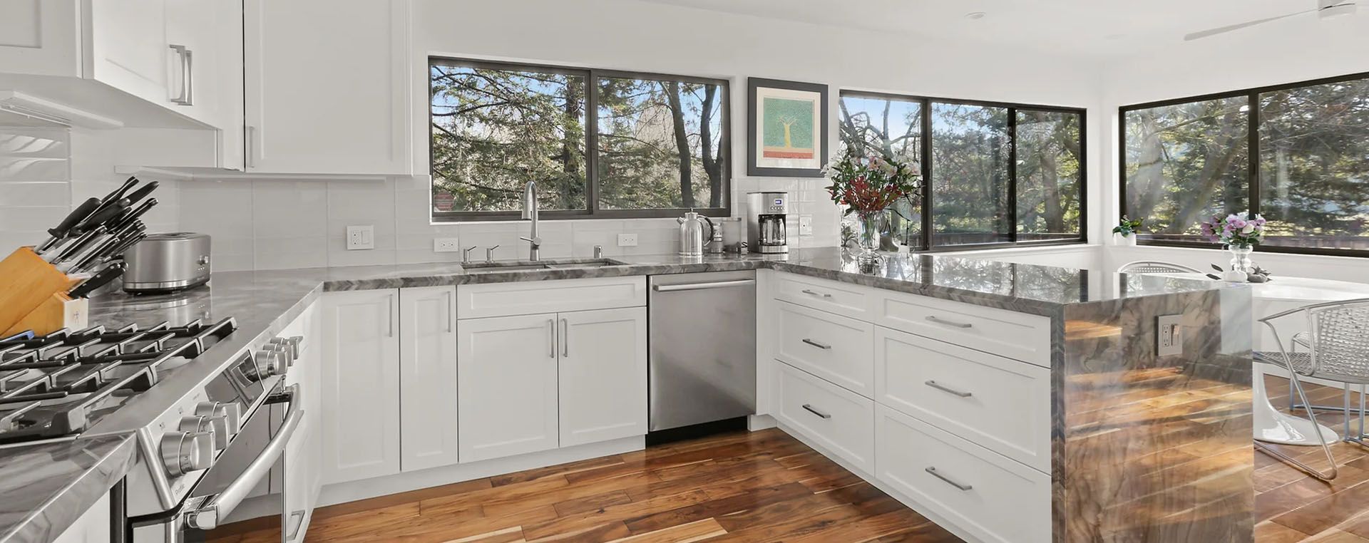 A kitchen with white cabinets , a stove , a sink , and a lot of windows.