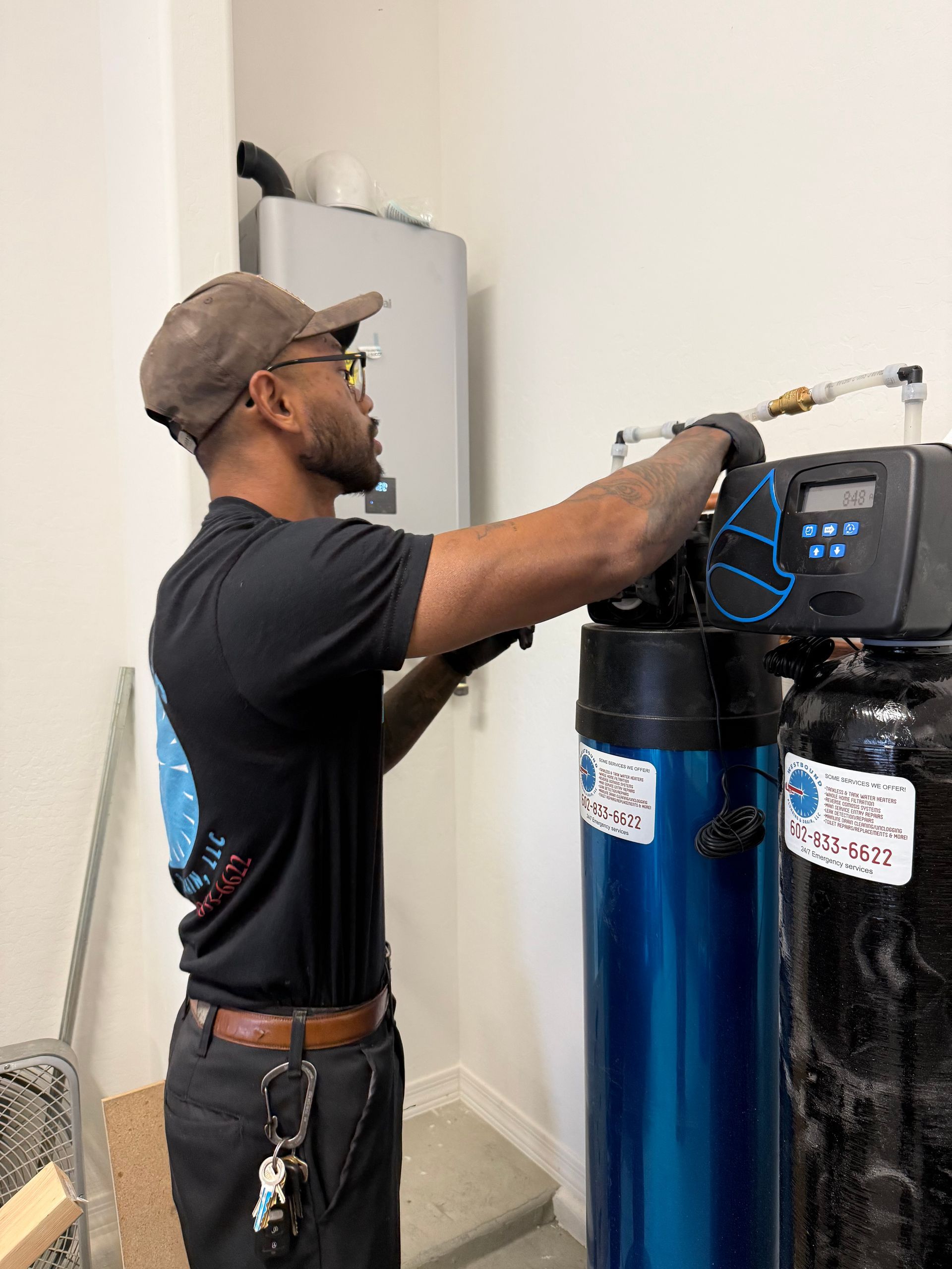 Plumber installs water filtration system. He wears a cap, glasses, and gloves, working on a blue and black tank.