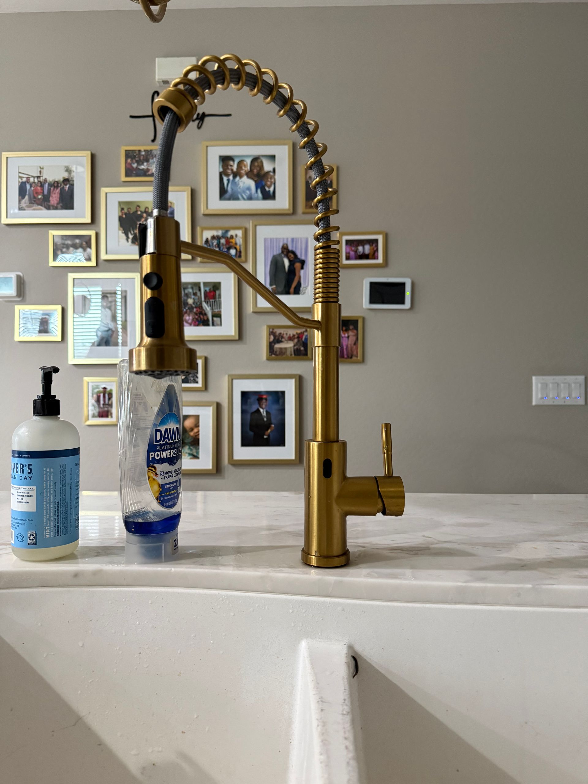 Gold kitchen faucet with soap and dish soap on a countertop. Family photos hang in the background.