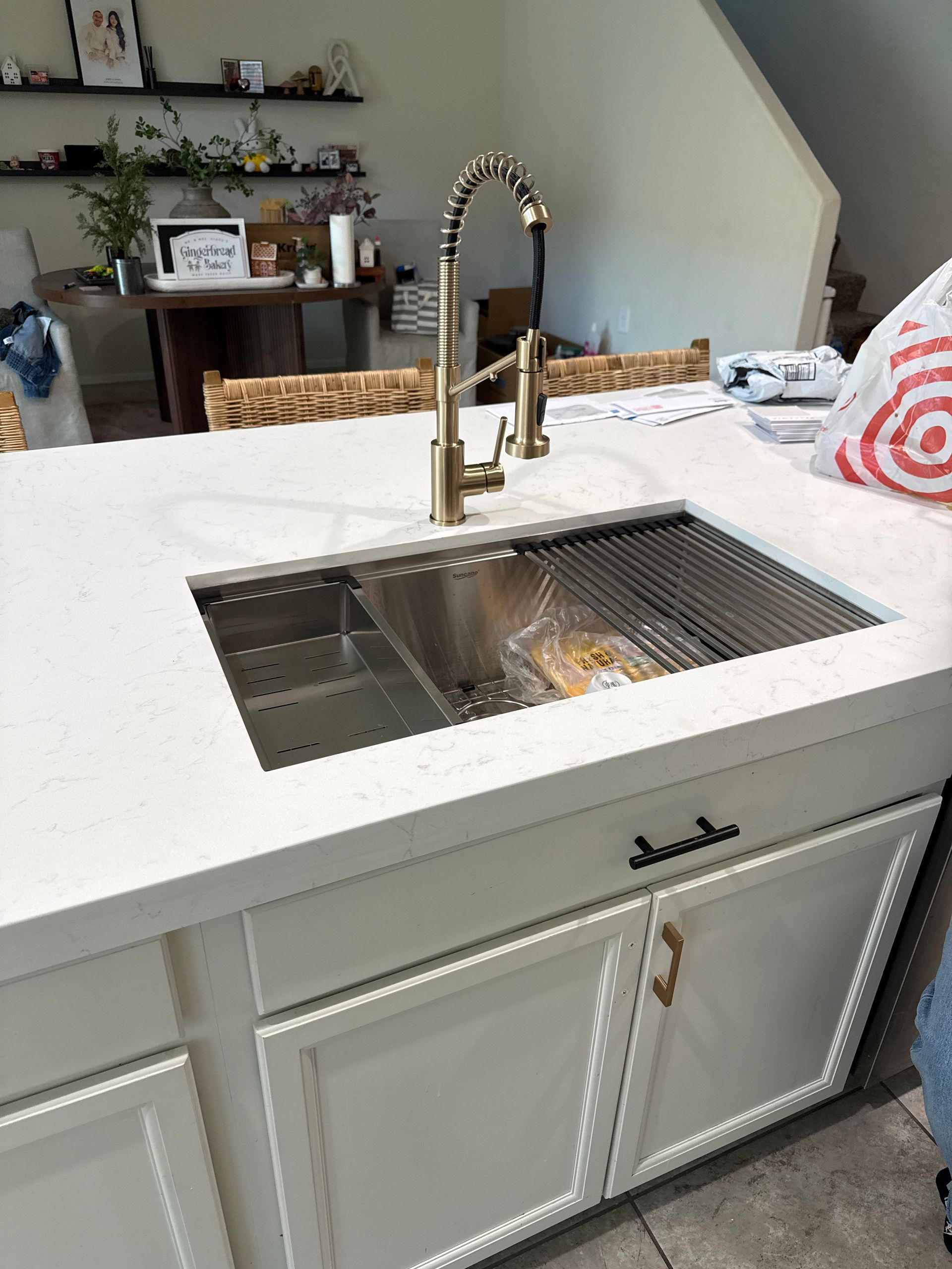 Kitchen island with a stainless steel sink, gold faucet, and white cabinets.