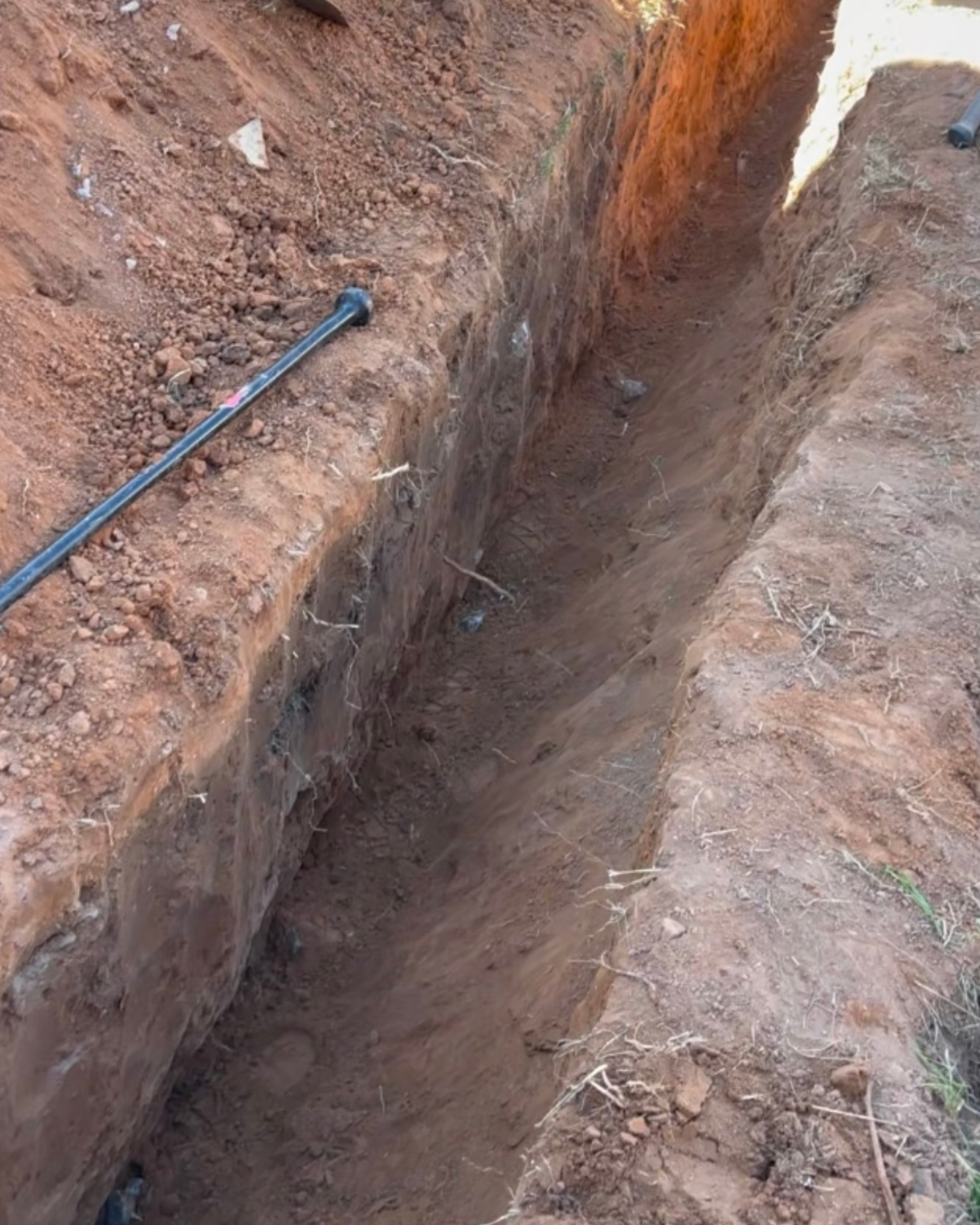 A hose is laying in the dirt next to a trench.