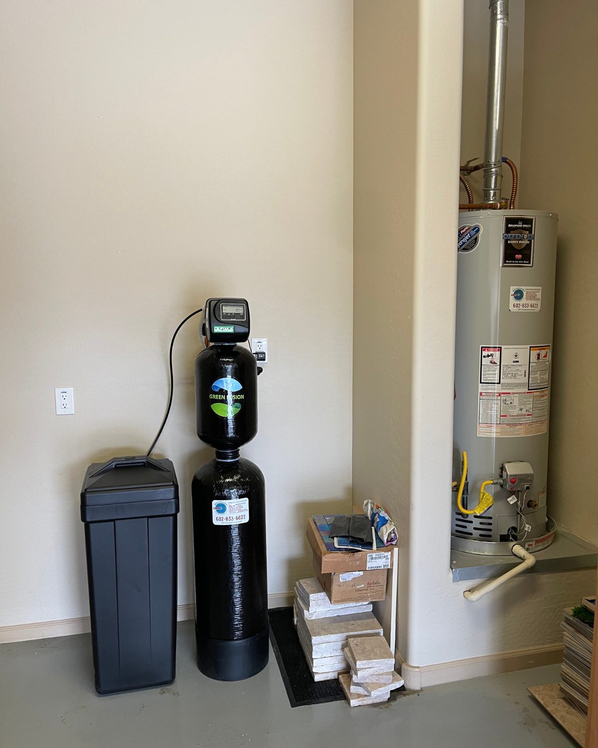 A water softener is sitting next to a water heater in a room.