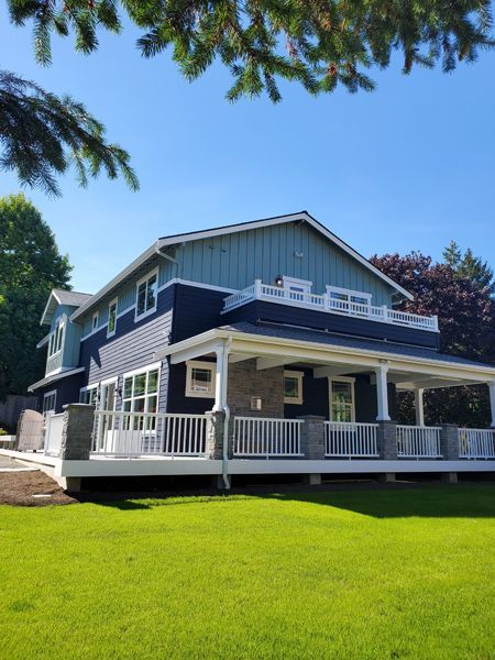 Two-story house with blue and white siding, large porch, on a green lawn under a blue sky.