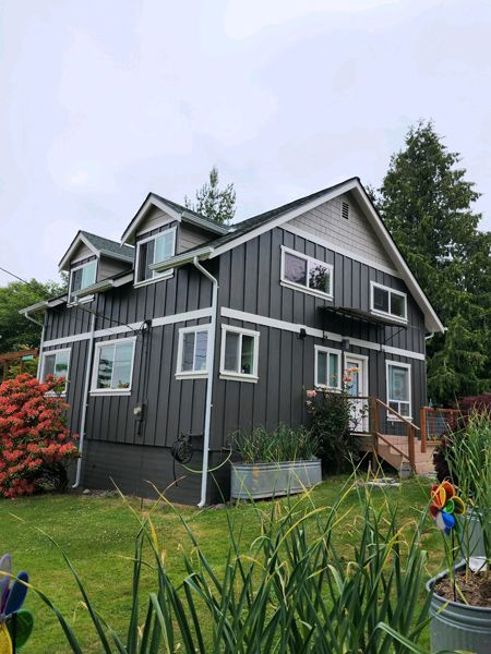 Two-story grey house with white trim, dormers, and a garden in the front yard.