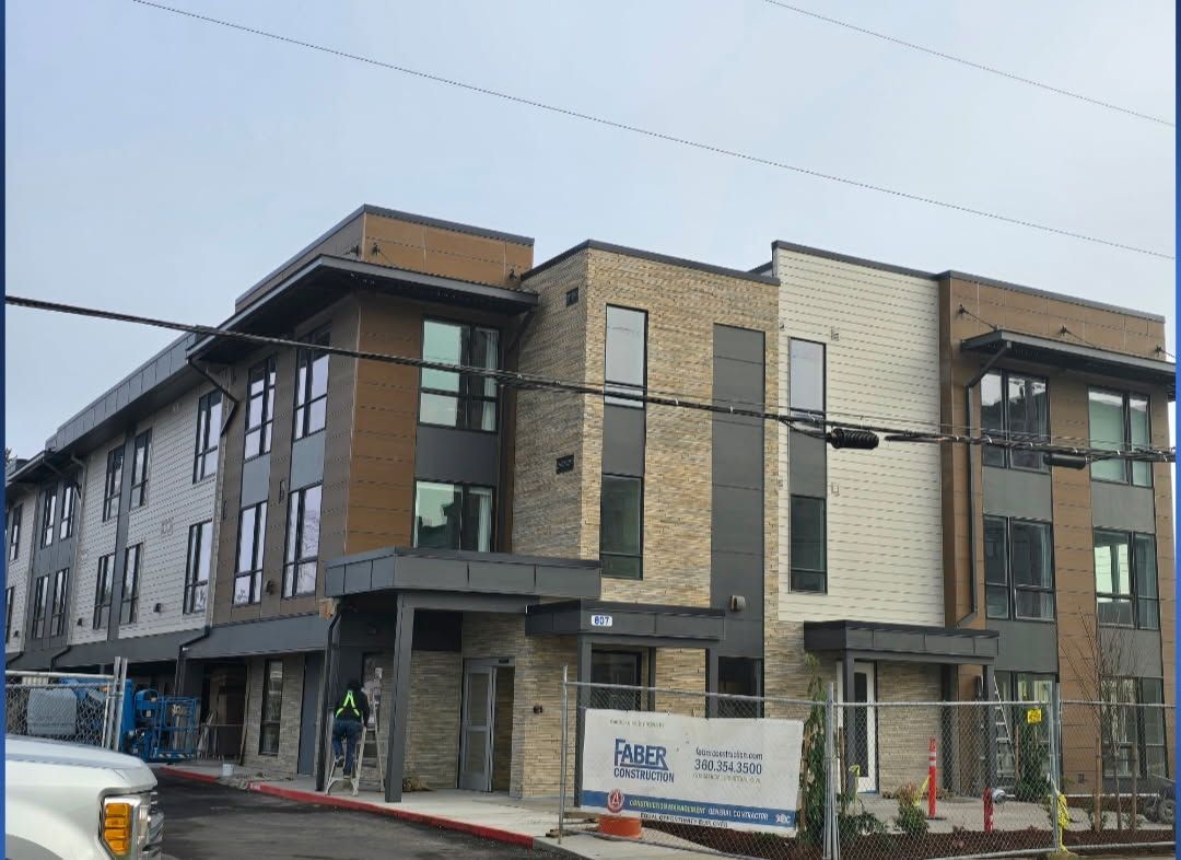 Three-story building under construction with varied brick and panel facades, sidewalk, utility pole wires.