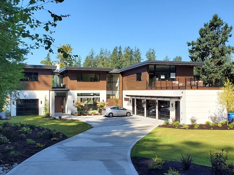 Modern home with a long driveway, a car, and a bright blue sky.