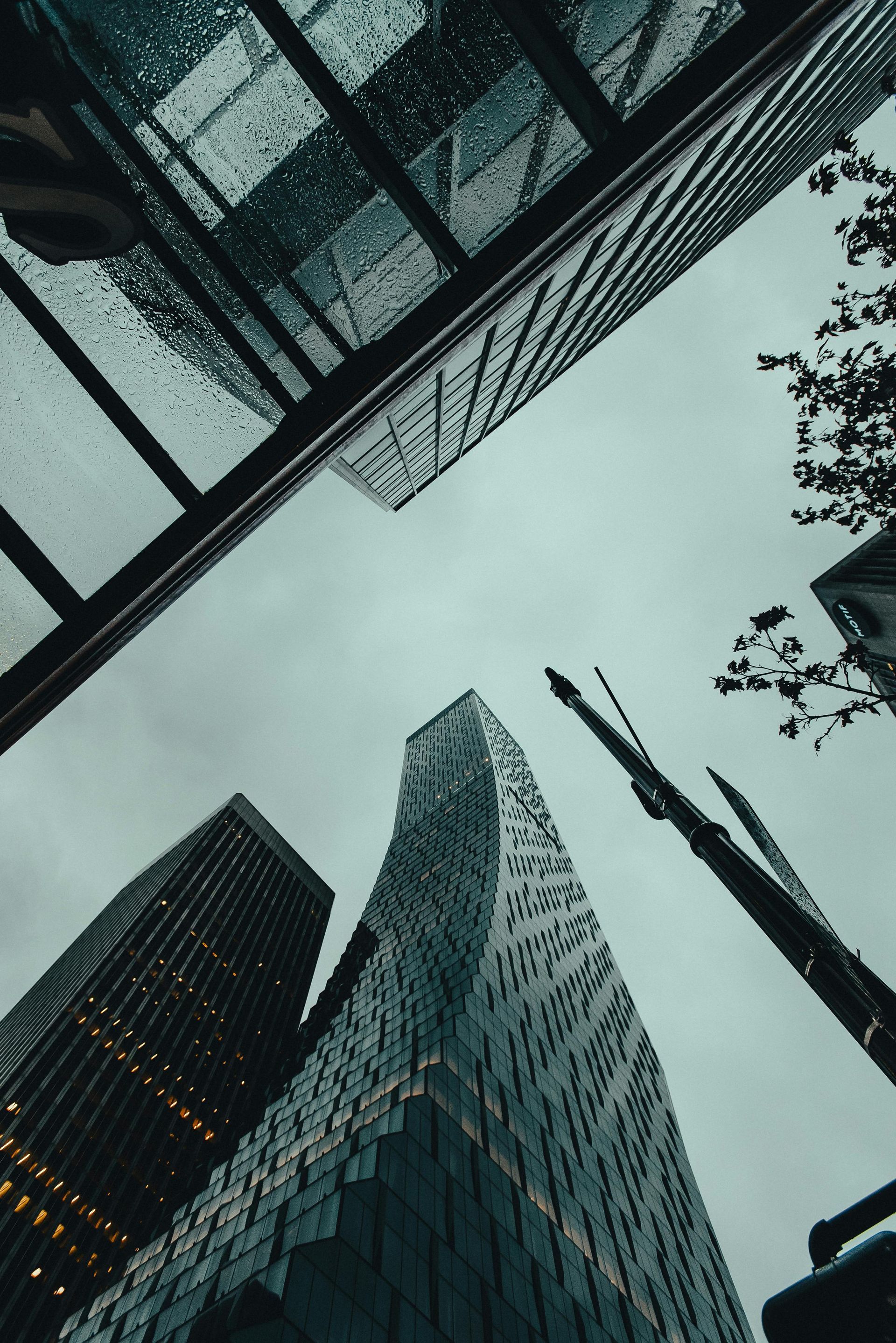 Low-angle shot of modern skyscrapers under a cloudy, gray sky. Dark, glass-clad buildings reach upward.