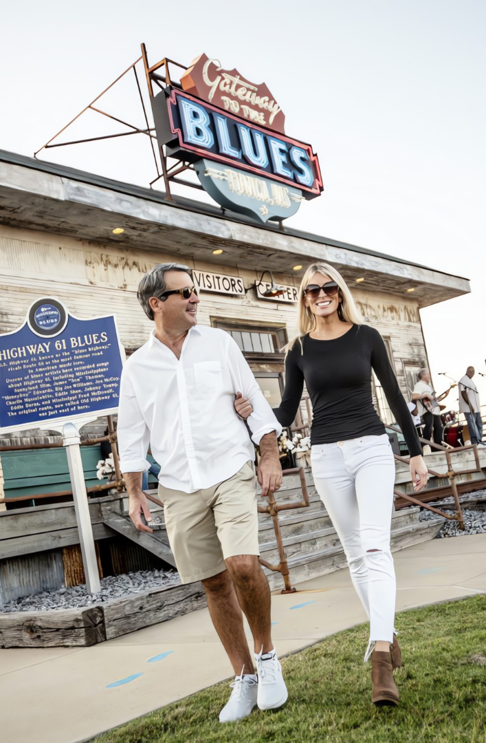 A man and a woman are walking in front of a building with a sign that says blues.