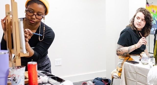 Two women are painting on an easel in a room.