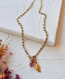 A gold necklace with a feather pendant is sitting on top of a white canvas.