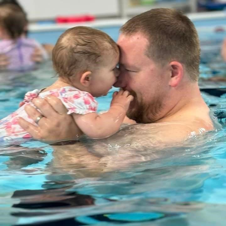 A man is holding a baby in a swimming pool.