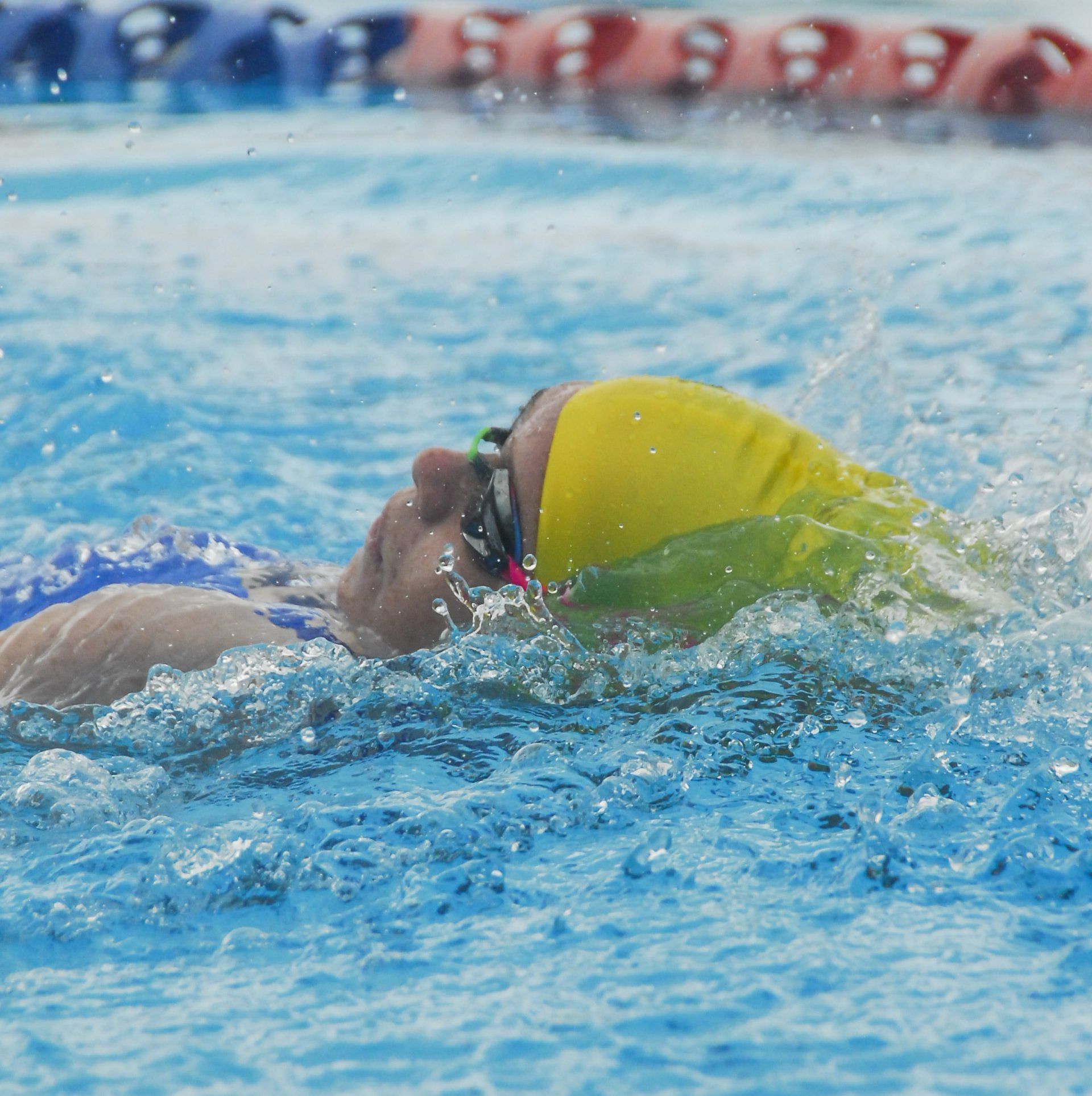 A person wearing a yellow swim cap and goggles is swimming in a pool.