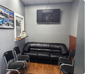 Waiting room: black leather sofa, four black chairs, TV on gray wall, picture, wooden floor.
