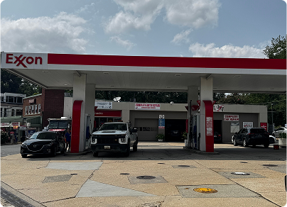 Exxon gas station with cars at the pumps under a red and white canopy on a cloudy day.