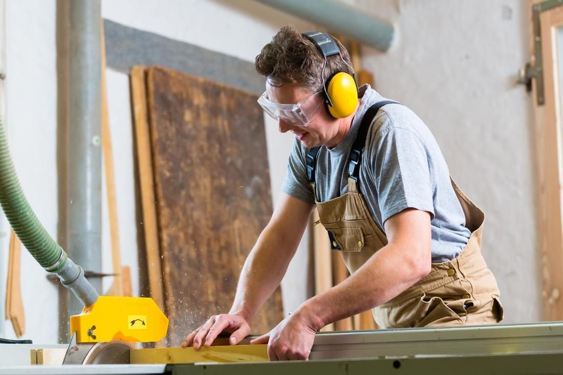 A man wearing ear muffs and goggles is cutting a piece of wood with a circular saw.