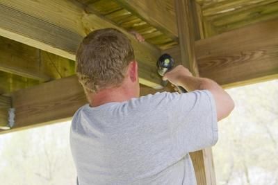 A man is working on a wooden structure with a drill.