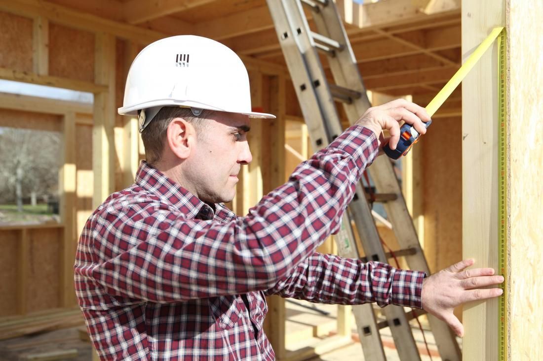 A man is measuring a piece of wood with a tape measure.