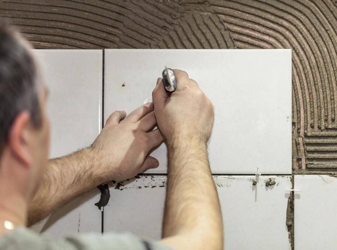 A man is installing tiles on a wall with a hammer.