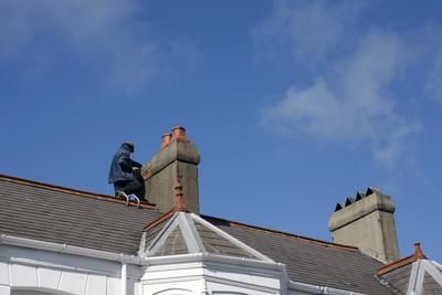 A man is sitting on top of a roof working on a chimney.