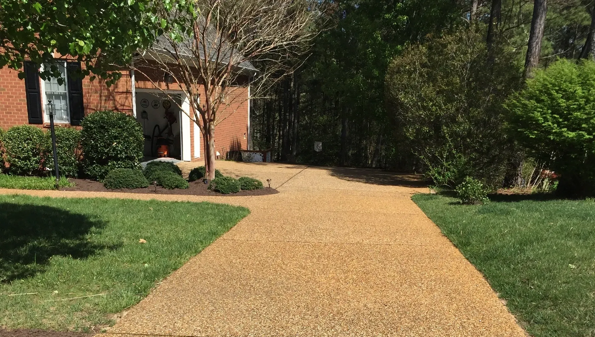 Driveway made of small beige stones leading to a brick house with green lawn.