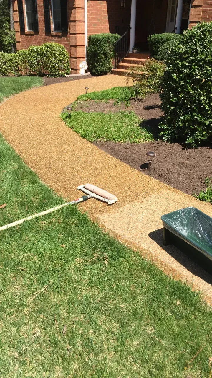 A person applying sealant to a gravel pathway with a brush in a sunny yard.