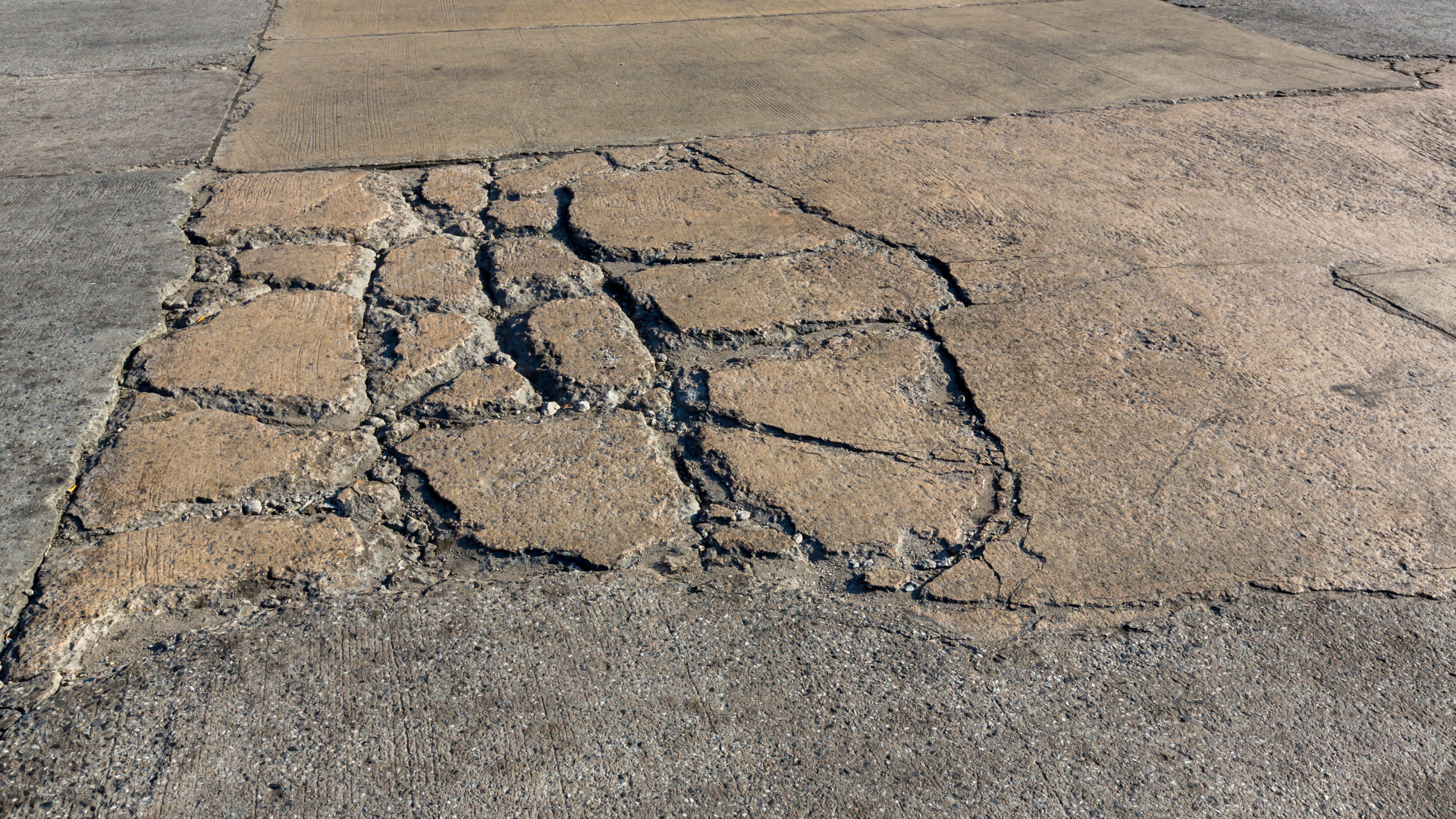 Cracked asphalt pavement with a large patch of broken, uneven road surface
