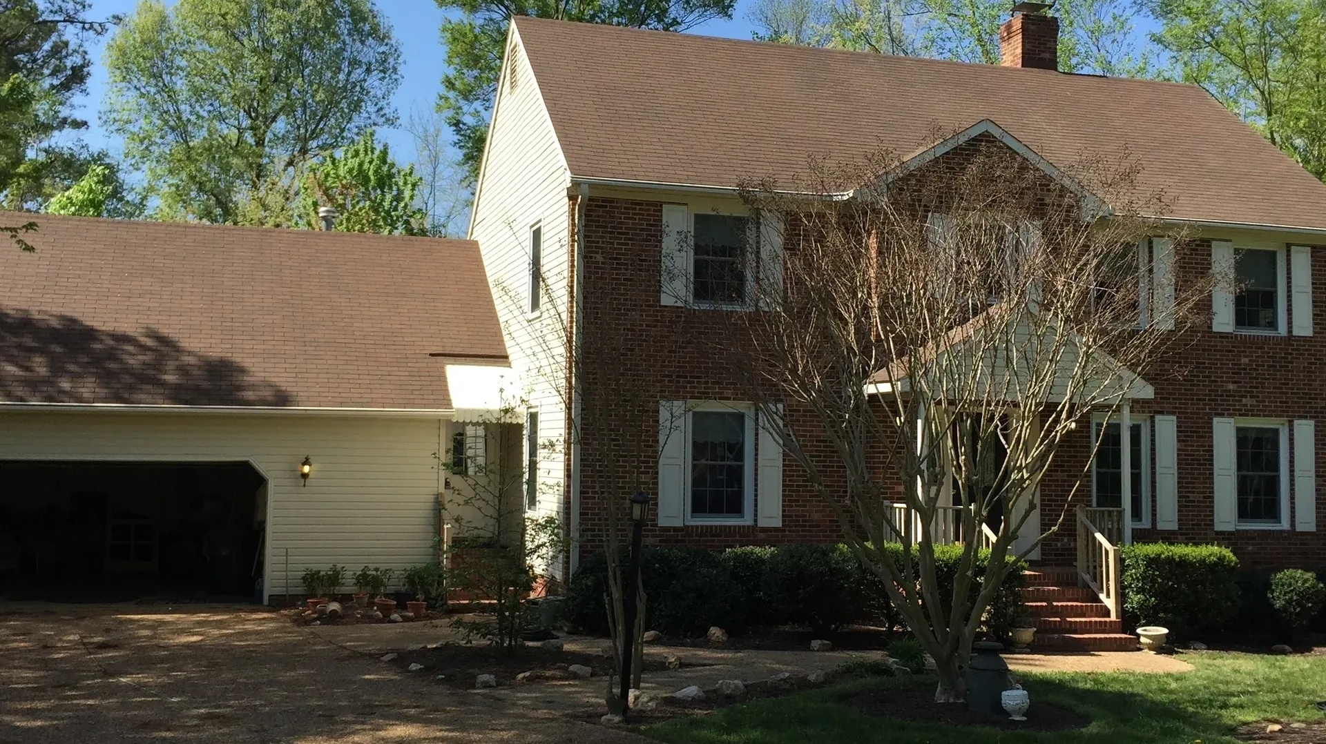 Two-story brick house with attached garage, brown roof, white shutters, and a front porch.