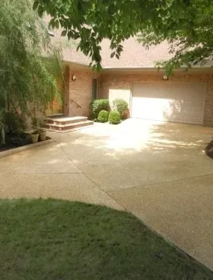 Driveway leading to a brick house with a garage and landscaping. Bright sunlight.