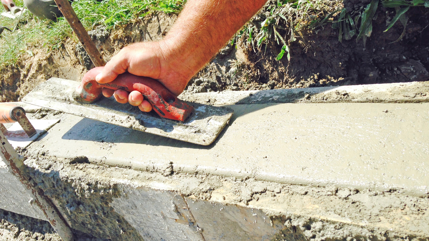 Person smoothing wet concrete with a trowel outdoors.