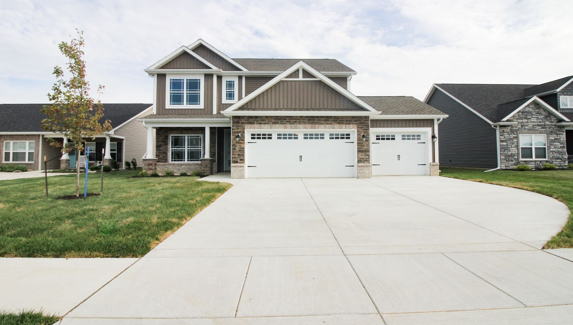 Two-story house with a light-colored driveway and lawn under a cloudy sky.