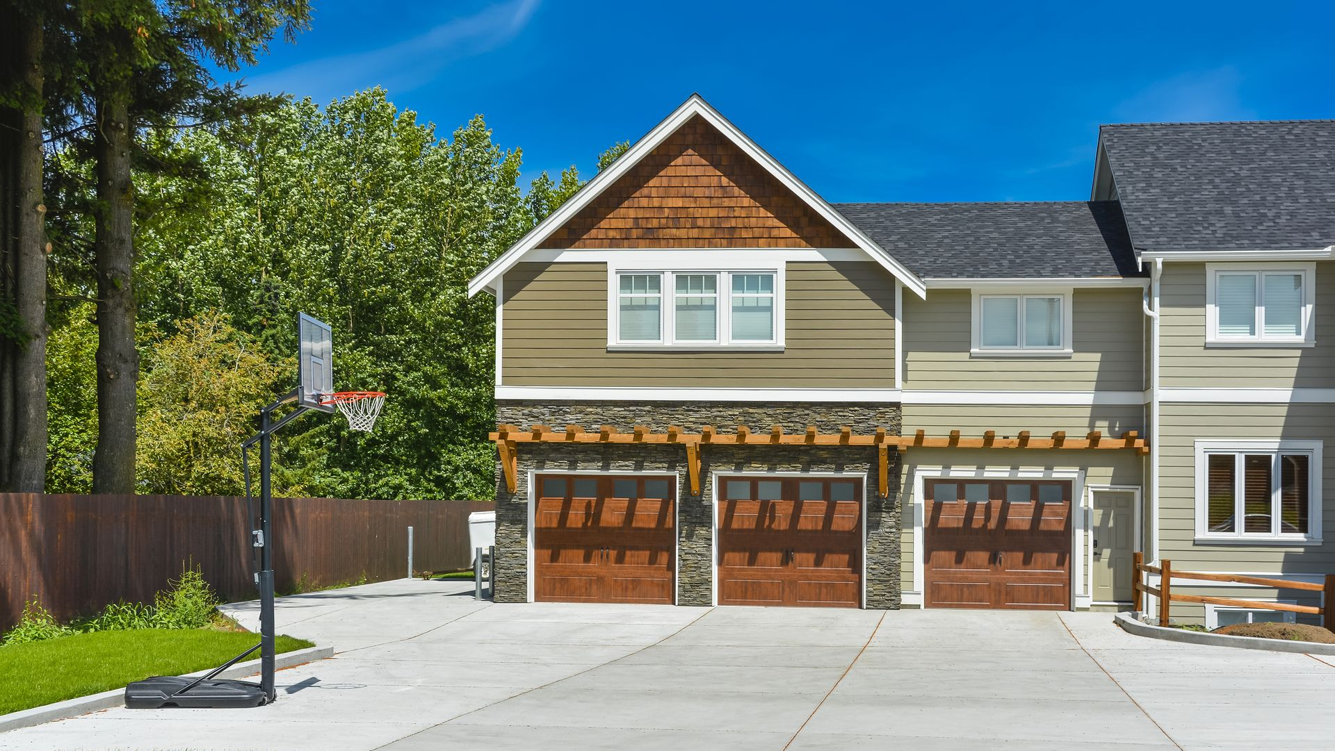 A three-car garage of a suburban home with a concrete driveway and a portable basketball hoop on the side.