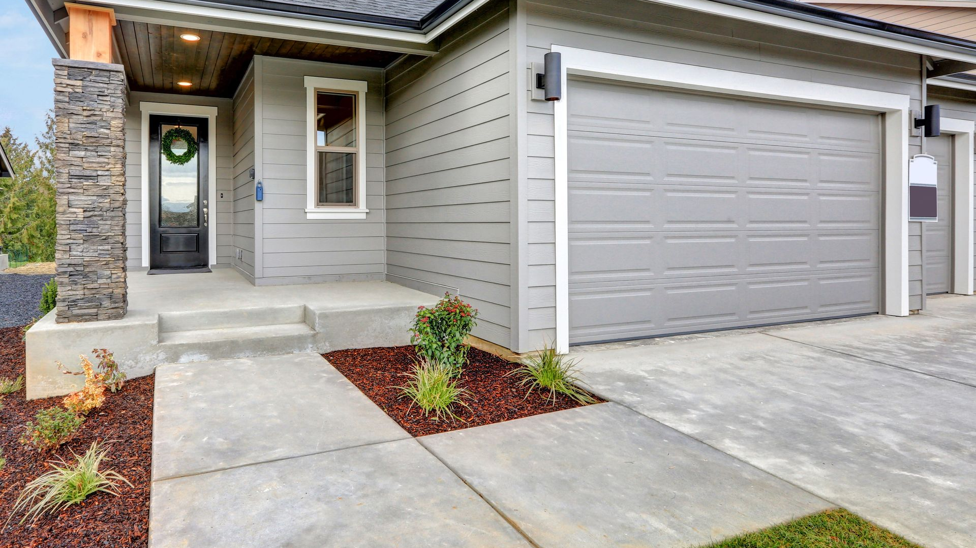 Modern gray house exterior with a stone pillar, front entry door, and a concrete driveway leading to a garage.