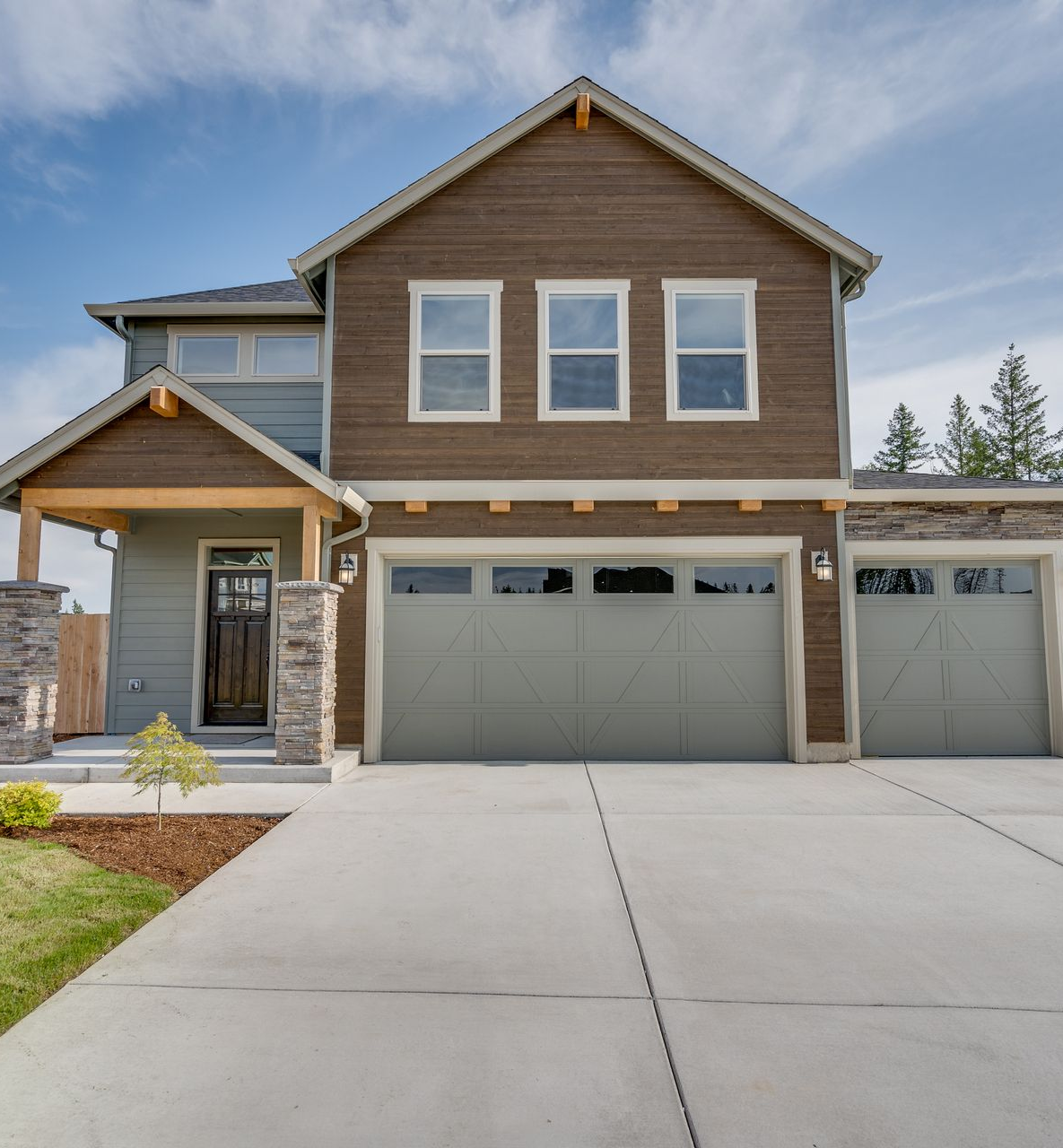 Two-story house with green and brown siding, a concrete driveway, and a two-car garage under a blue sky.