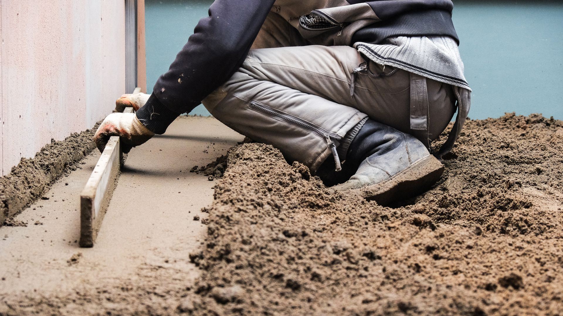 Worker smoothing wet concrete beside a wall with a trowel outdoors