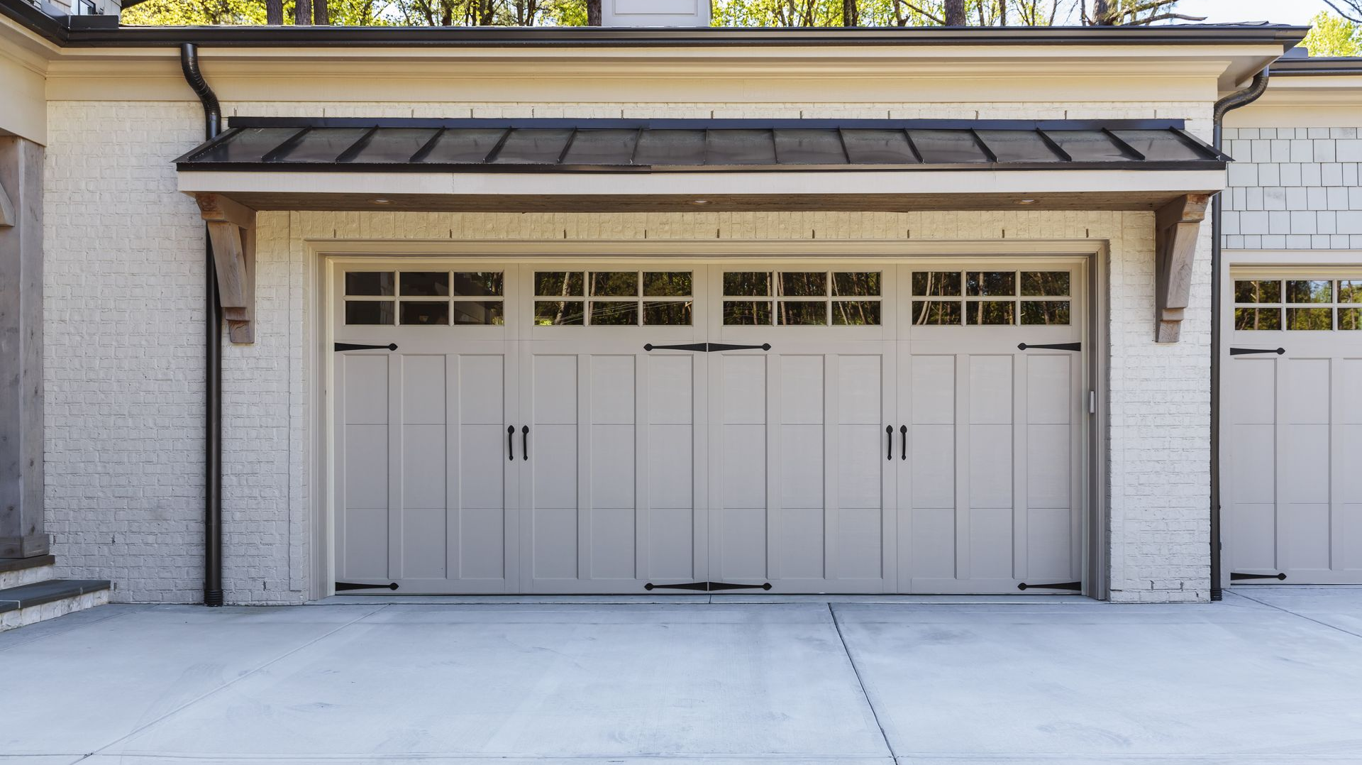 Beige garage doors with decorative black hardware under a dark roof, concrete driveway.