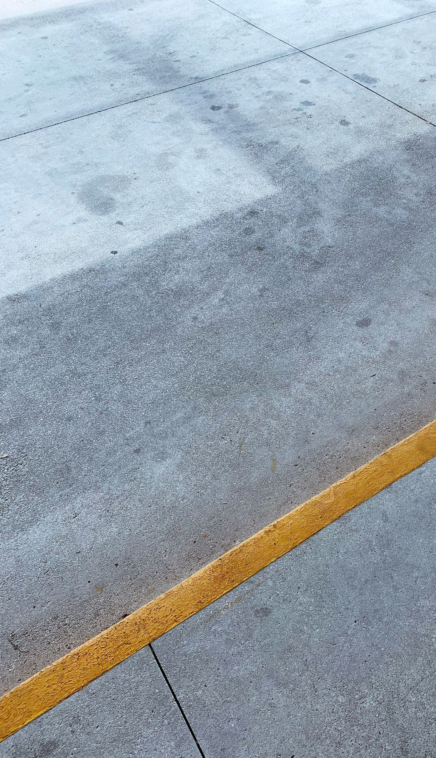 Close-up of a gray concrete surface with a yellow painted line running diagonally across it.