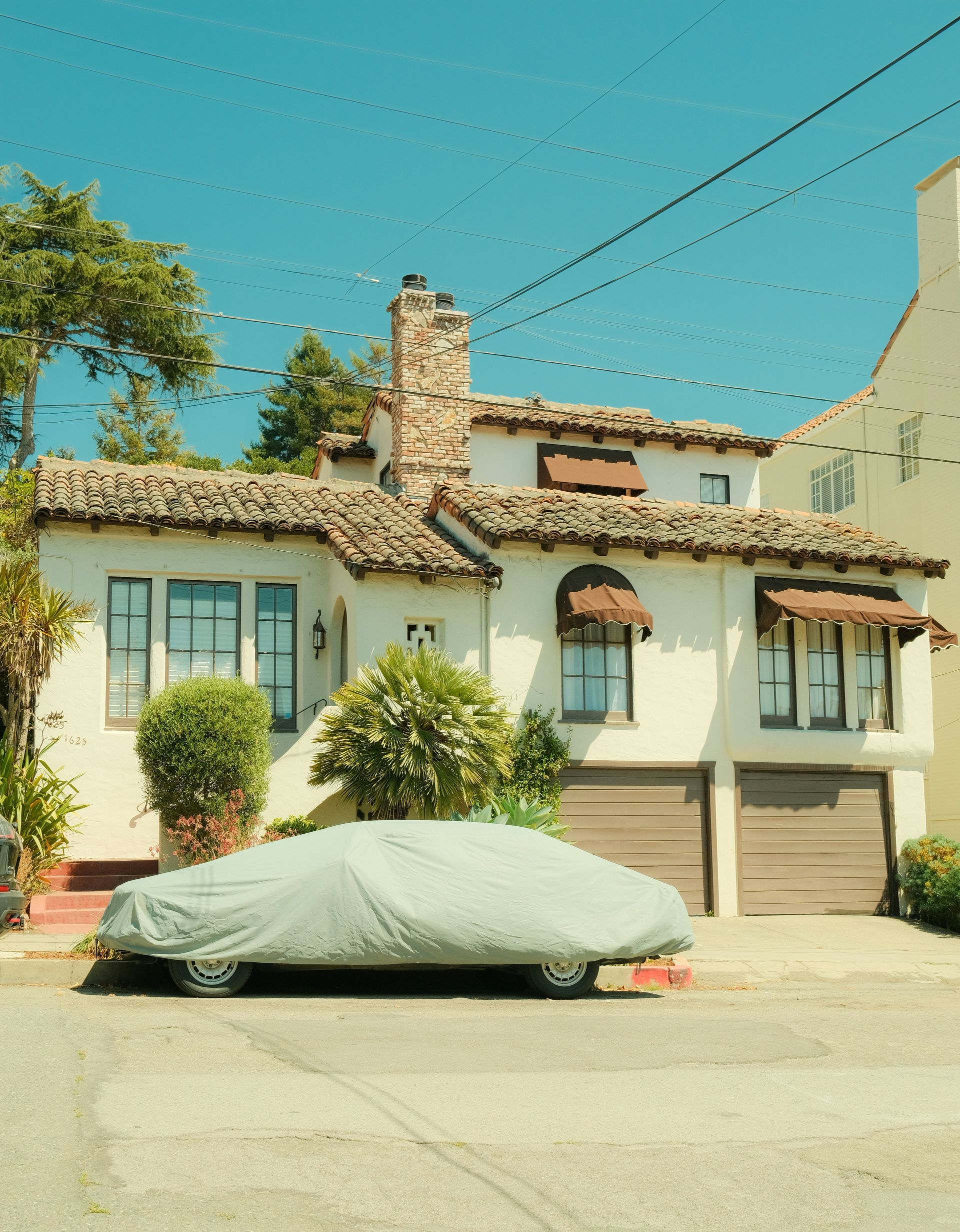 A two-story stucco house with a car covered by a tarp in front. Blue sky.