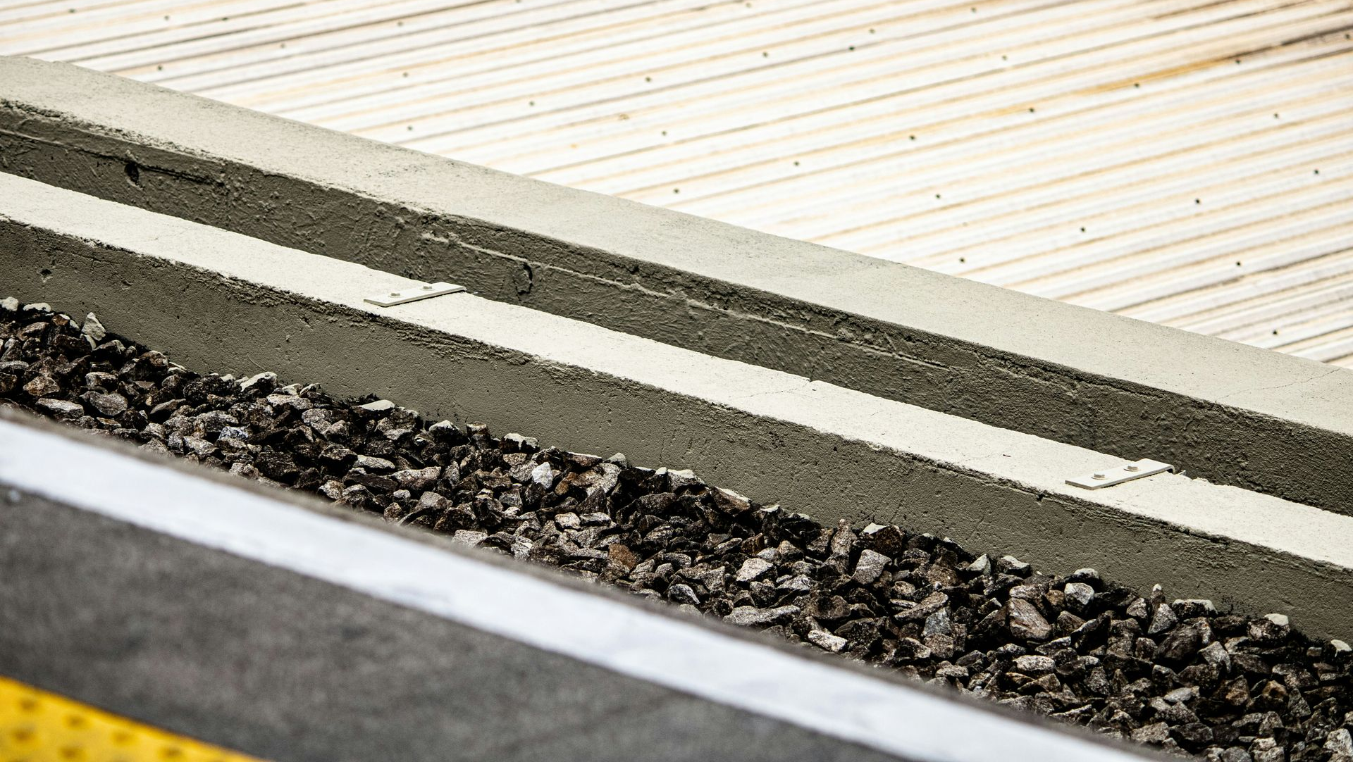 Rail platform edge with tactile paving, gravel, and striped safety lines