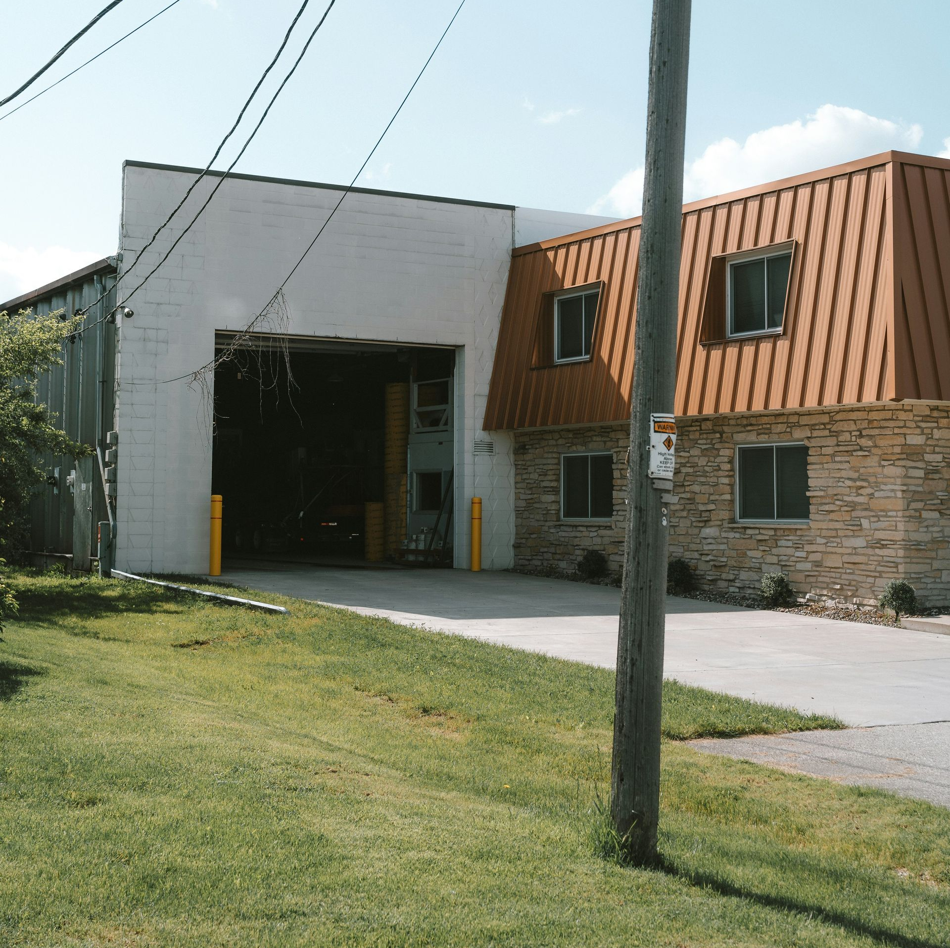 A building with an open garage bay, brown roof, and brick facade on a sunny day.