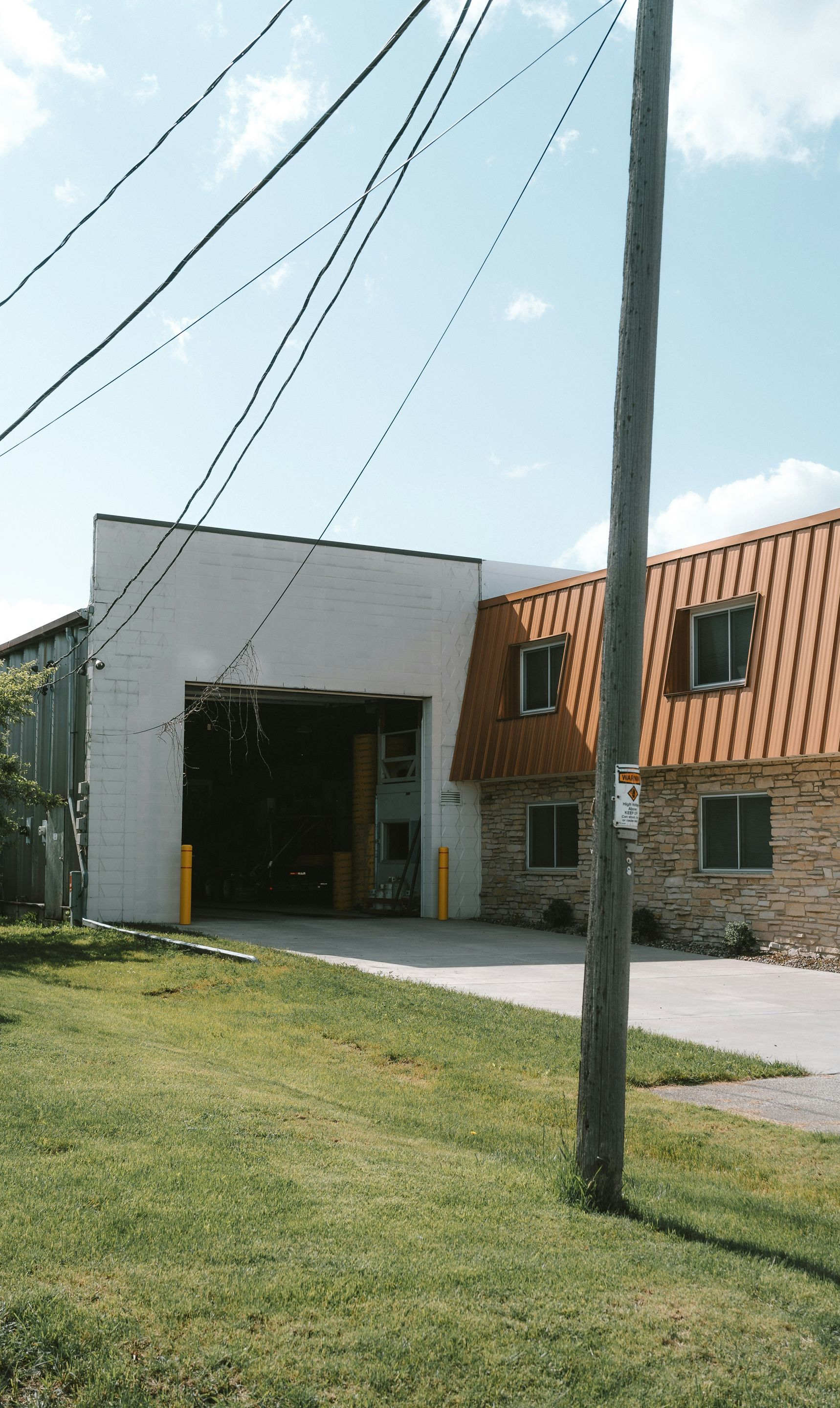 Garage building with open bay door, brown roof, and brick facade. Utility pole in foreground.