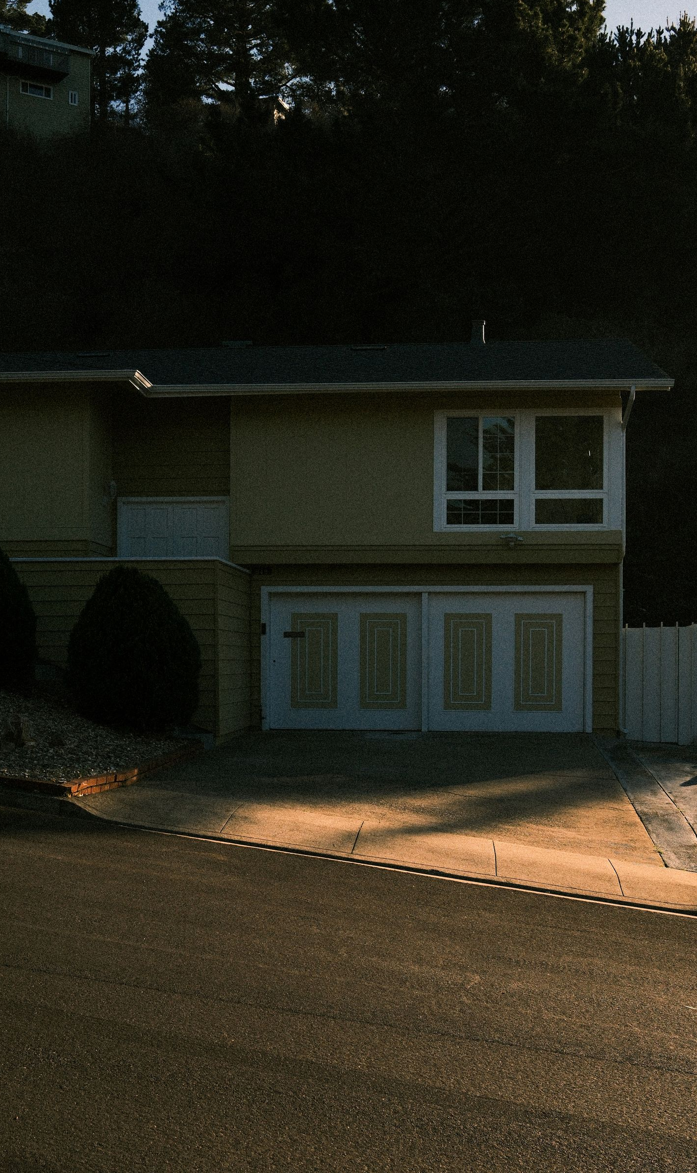Two-story house with white trim, garage doors, and windows, set against a dark hillside.