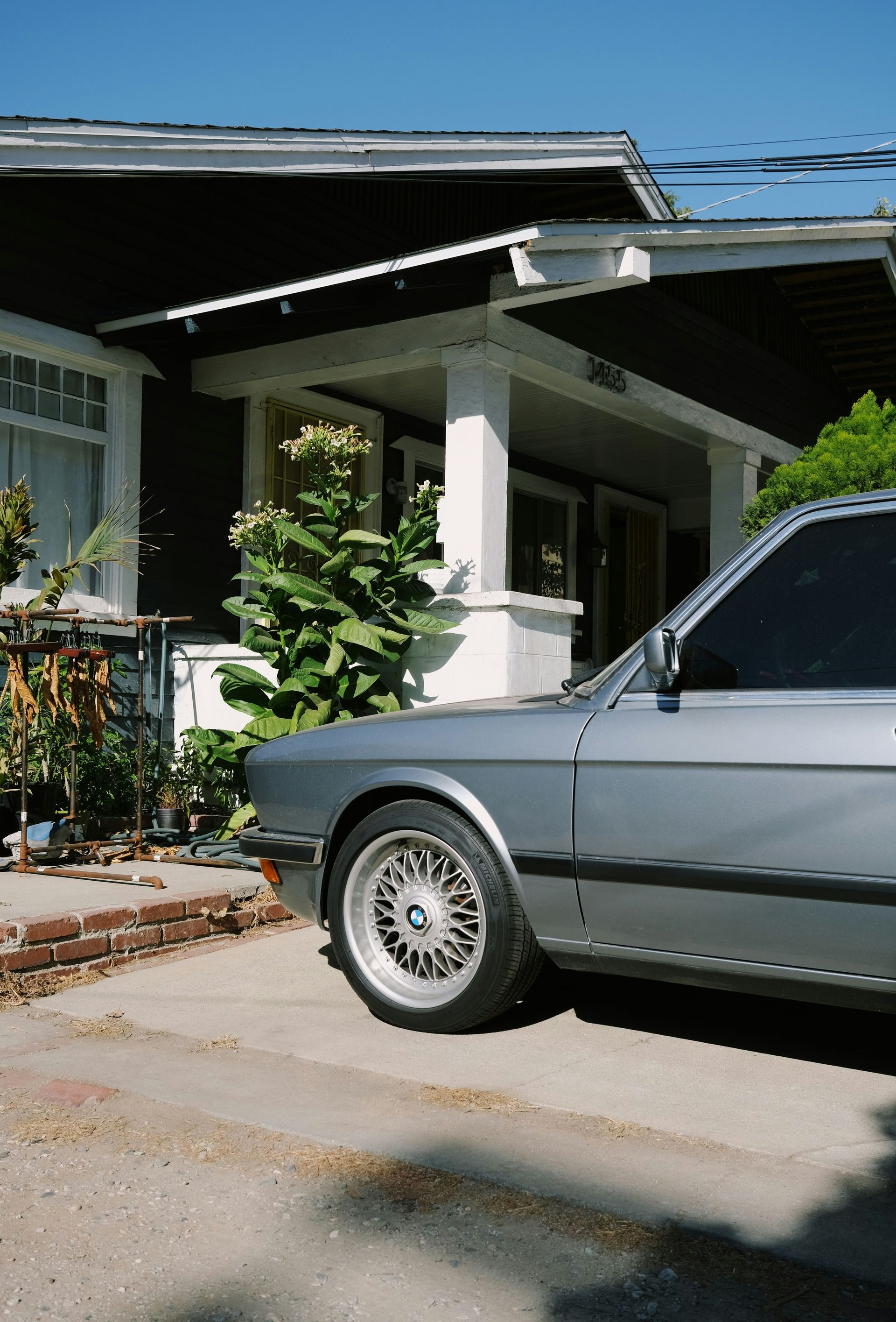 A silver BMW sedan with multi-spoke wheels parked on a driveway in front of a house with a porch.