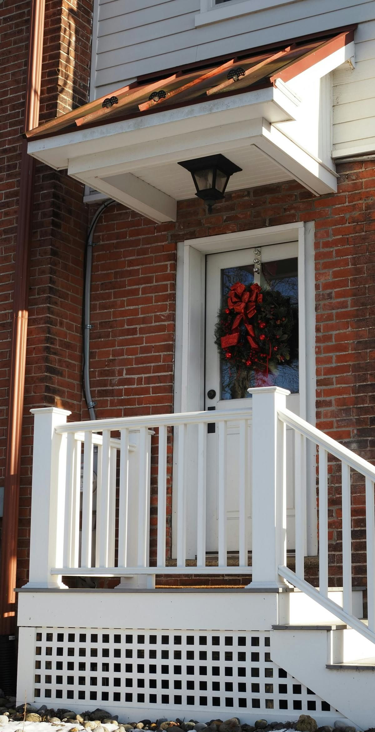 White porch with railing and brick exterior. Christmas wreath hangs on the front door.