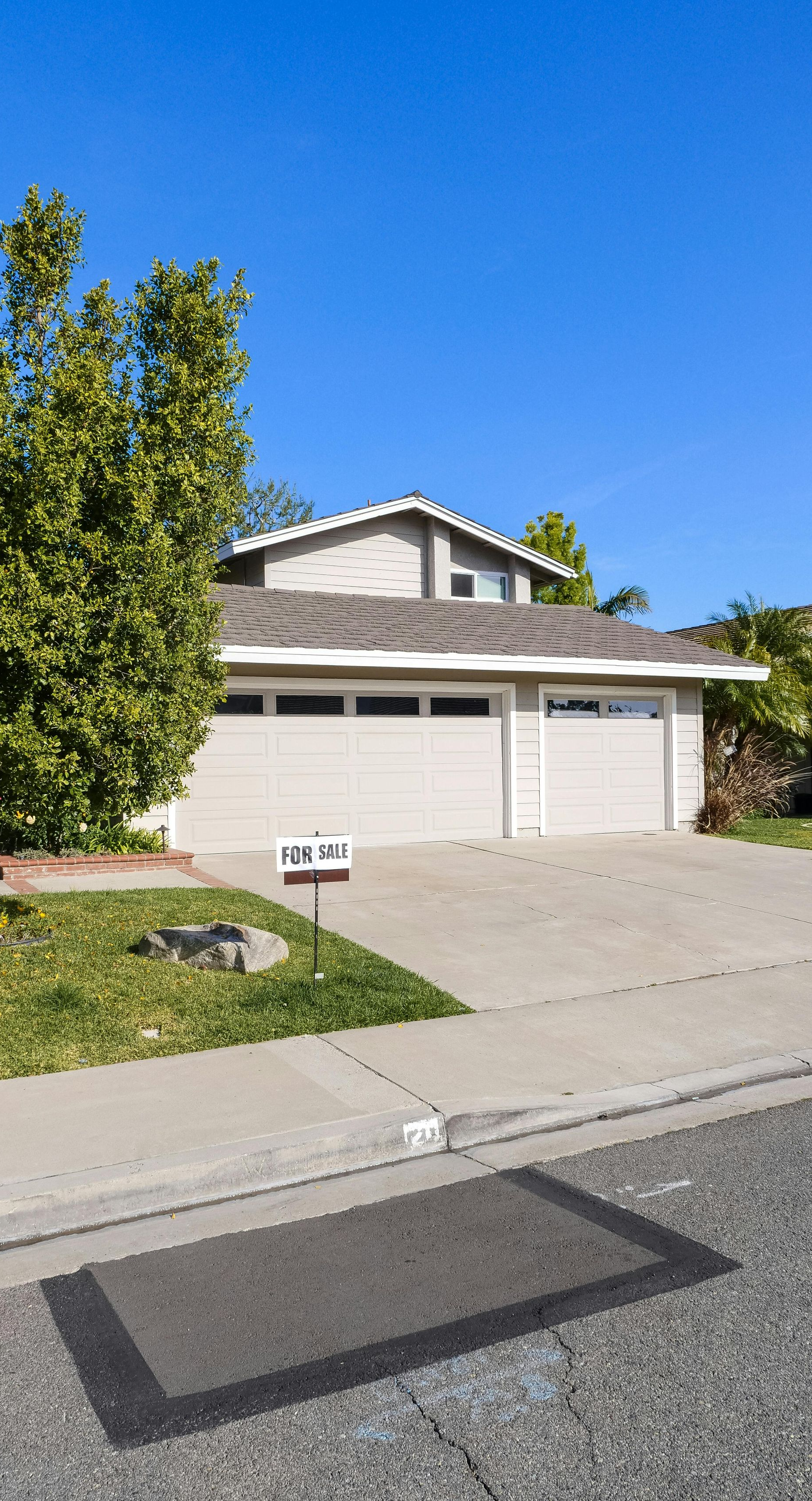 Two-story house with a light gray garage door, a driveway, and a tree on a sunny day.