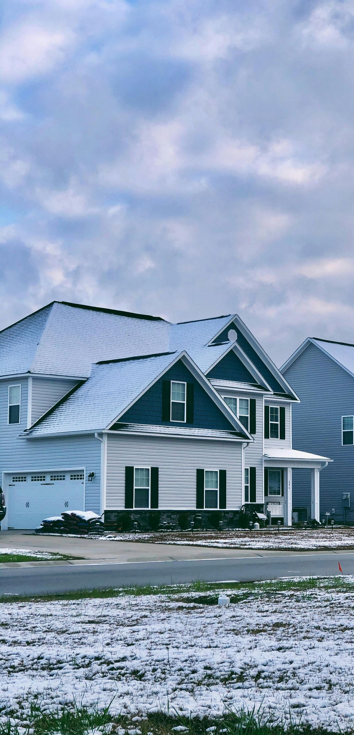 Houses with snow-covered roofs and a snow-covered lawn against a cloudy sky.