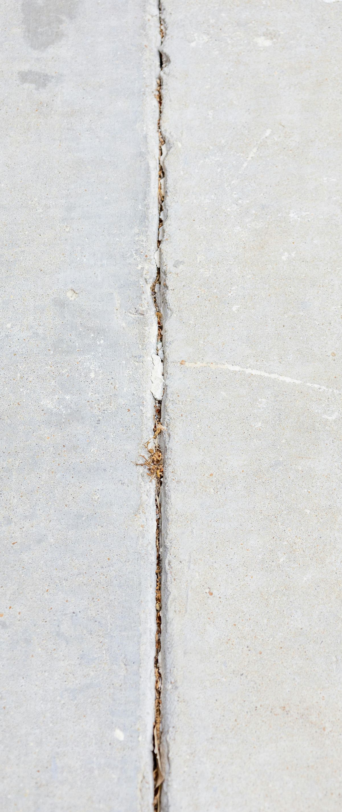 Crack in a light gray concrete wall with rust stains along the seam