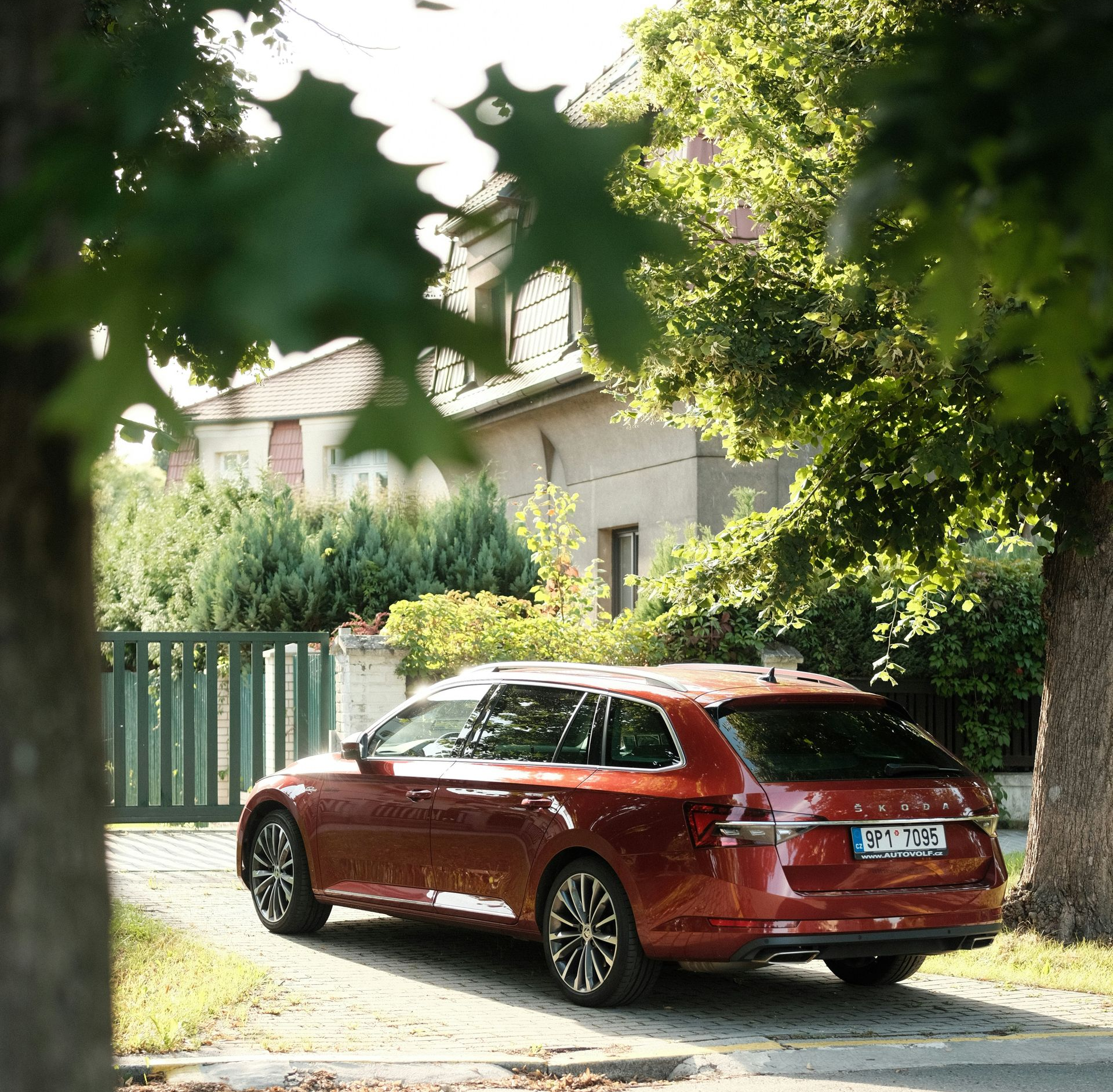 Red station wagon parked on a driveway in front of a house, framed by trees.