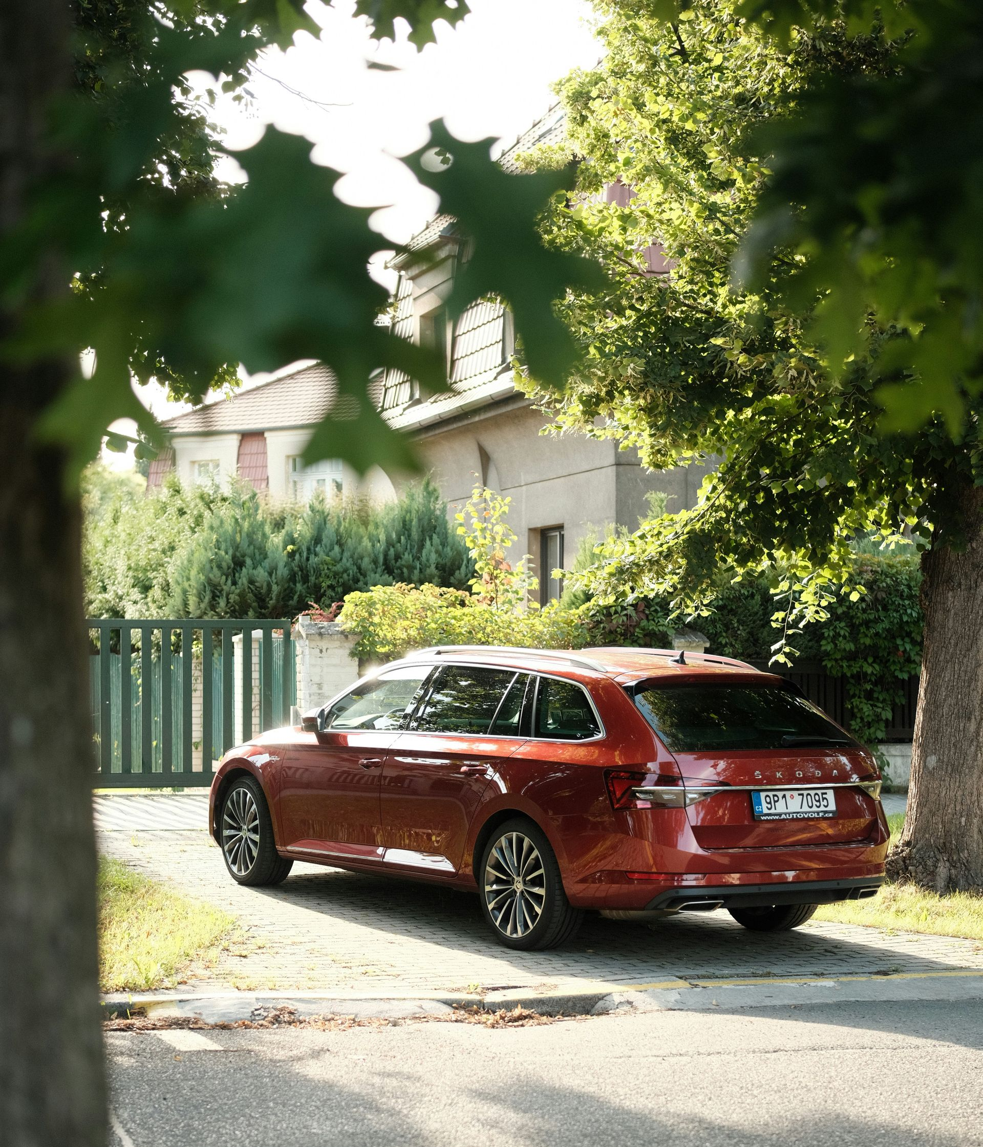 Red station wagon parked in front of a house, seen through tree branches. Sunny day.