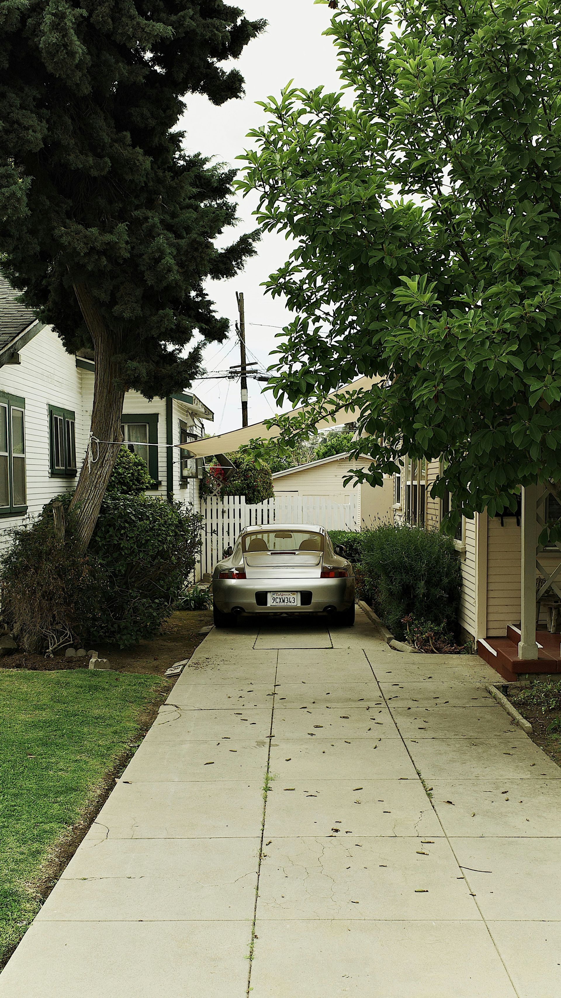 Silver car parked in a narrow concrete driveway between houses with trees and greenery.
