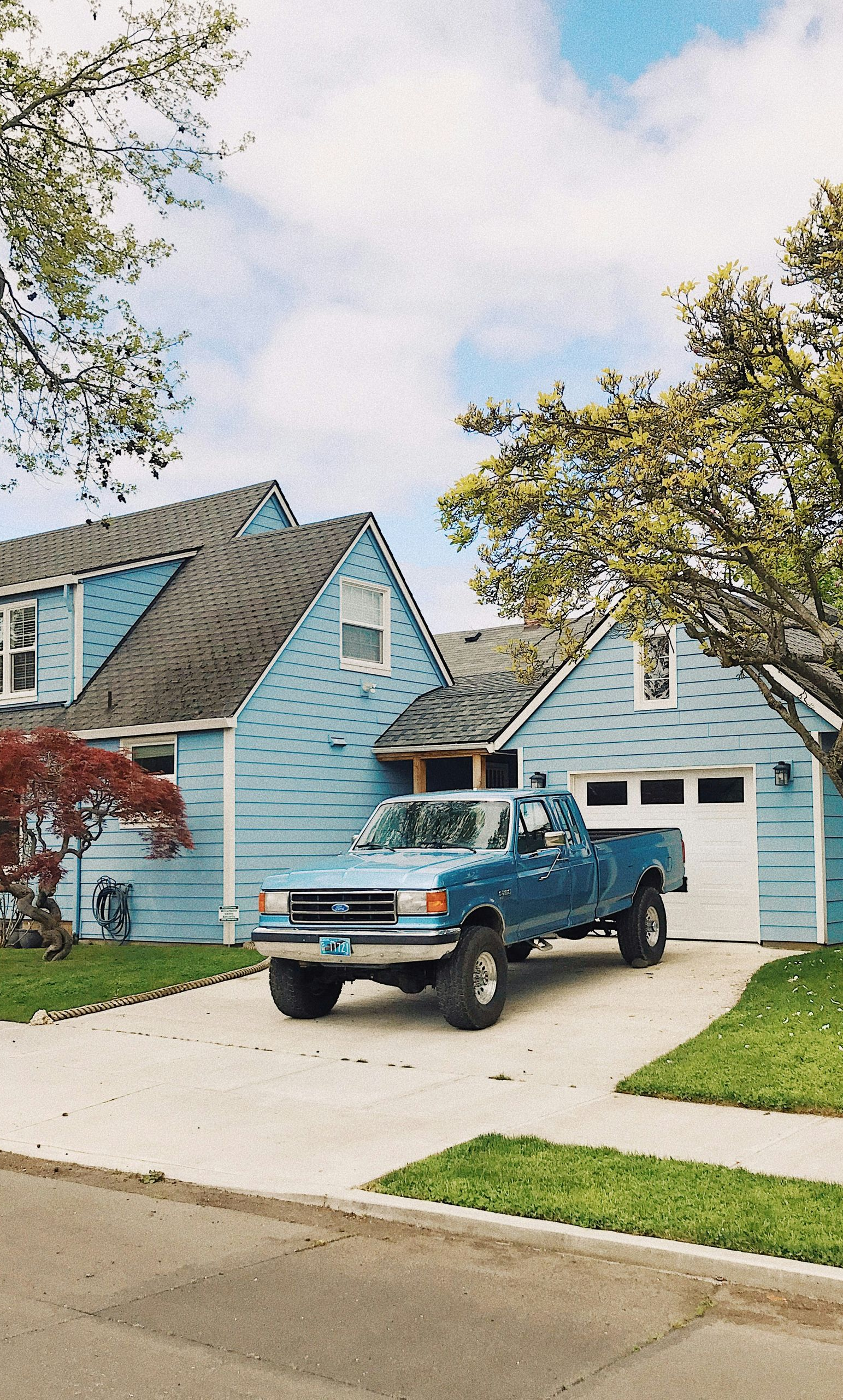Blue pickup truck parked in front of a blue house with white garage door and green yard.